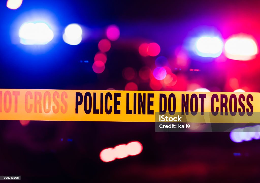 Accident or crime scene cordon tape, police line do not cross. It is nighttime, emergency lights of police cars flashing blue, red and white in the background
