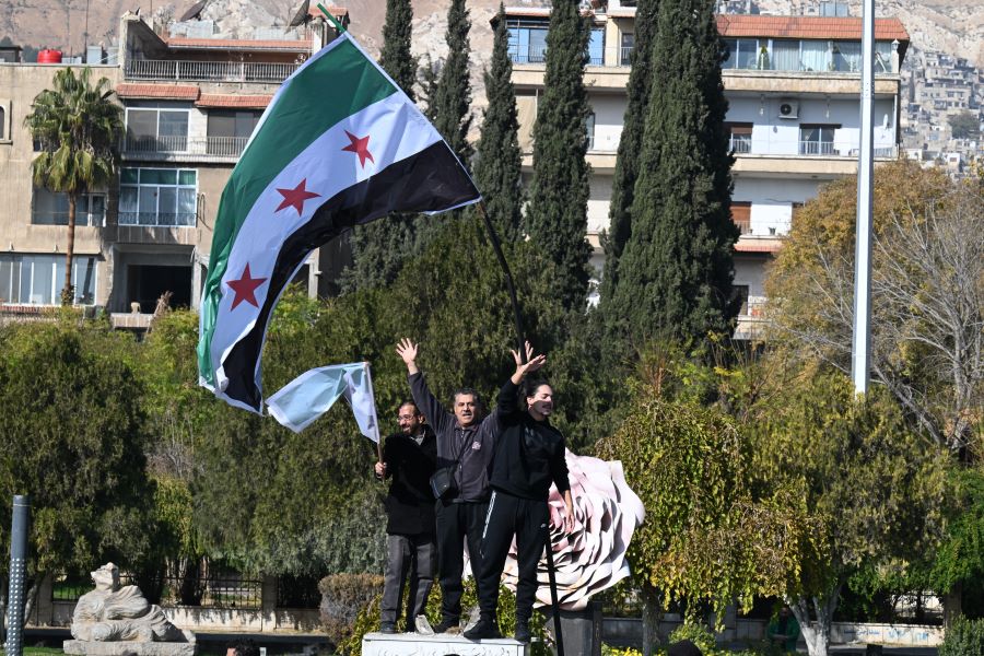 Syrian men wave the flag of the opposition as they stand where the statue of a Syrian soldier was brought down by rebels in the central Umayyad Square in Damascus on Monday. Photo AFP/Louai Beshara