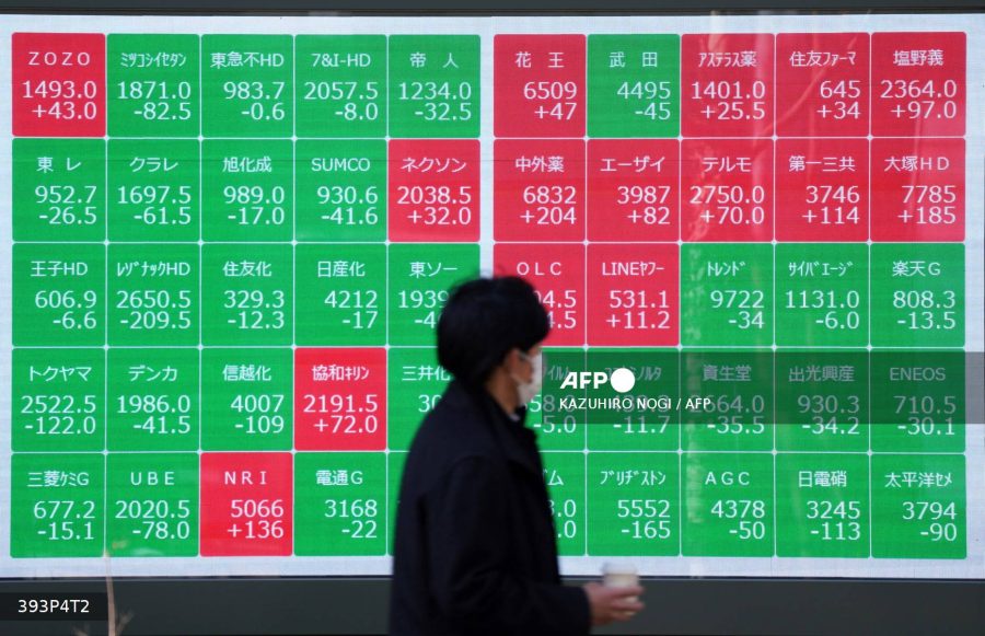 A man walks past an electronic board showing the Nikkei 225 index on the Tokyo Stock Exchange along a street in Tokyo