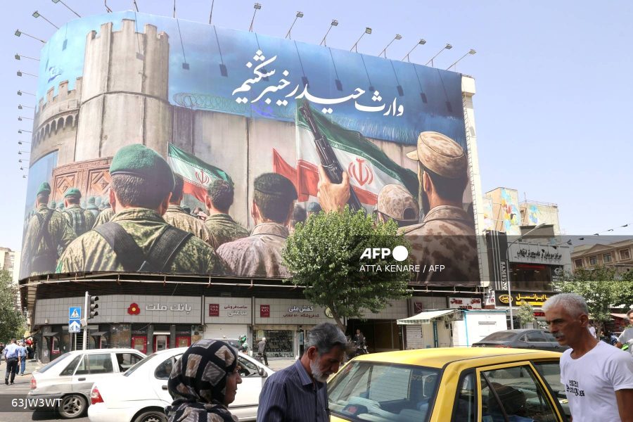 Caption: People walk past a huge banner on Enghelab (Revolution) Square, in Tehran on June 24, 2025. Iranian media on June 24, said an overnight Israeli strike on the north of the country killed nine people, ahead of US President's announcement of the start of a ceasefire between Israel and Iran.